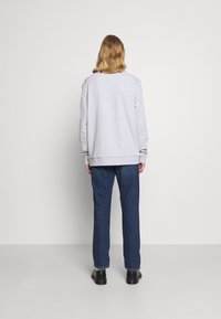 Sudadera gris de manga larga, con puños acanalados y un corte recto, combinada con jeans azul oscuro y zapatos negros. Diseño simple y casual.