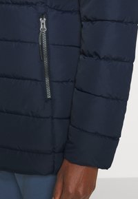 Doudoune bleu marine avec un design matelassé, dotée d'une fermeture éclair argentée et d'un tissu texturé. Les poignets élastiques complètent le design des manches.