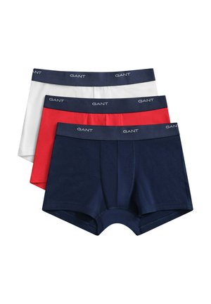 Jeune homme aux cheveux courts et foncés portant un boxer bleu marine GANT, debout devant un fond clair uni, face à l'avant.