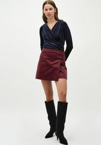 Mornarsko modra žametna zgornja majica z dolgimi rokavi v kombinaciji z burgundskim kordurojskim mini krilom, ki ima gumbe ob strani. Črne gambe iz semisue s višino nad koleni.