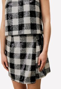 Ensemble deux pièces noir et blanc à sequins, comprenant un haut court et une mini-jupe avec un motif à damier et un design superposé.