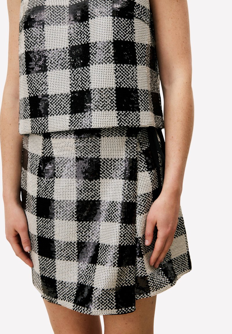 Ensemble deux pièces noir et blanc à sequins, comprenant un haut court et une mini-jupe avec un motif à damier et un design superposé.