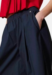 Pantaloni navy in tessuto con cintura elastica, pieghe frontali e tasche laterali. Presenta una piccola 'A' ricamata sulla cintura.