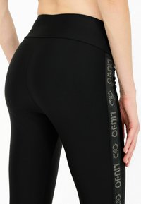 Leggings neri realizzati in un tessuto liscio ed elastico. Presentano una vita alta e un pannello laterale con dettagli di branding riflettenti.