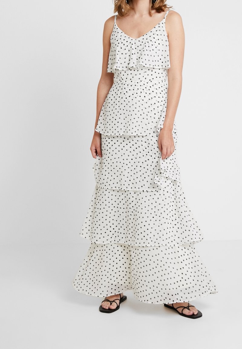 Vestido maxi blanco en capas con lunares negros, con capas con volantes y tirantes finos. Estilizado con sandalias planas negras.