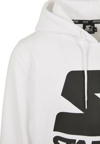 Sweat à capuche blanc avec un grand logo étoile graphique noire sur la poitrine et des cordons blancs sur la capuche.