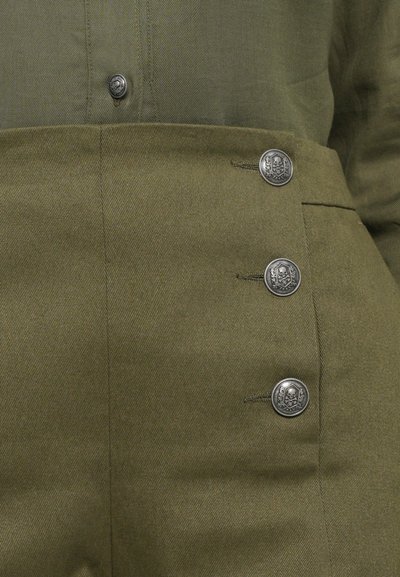 Olive zelene hlače z gladko teksturo, ki imajo tri kovinske srebrne gumbe okrašene z dizajnom lobanje. Prilagojen pas, strukturirana prilagoditev.