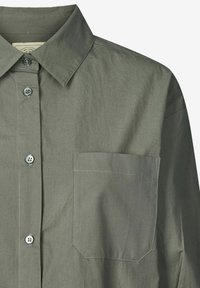Camicia con bottoni in un tessuto verde tenue, caratterizzata da un colletto classico, tasca frontale e bottoni lucidi, con una finitura liscia e testurizzata.