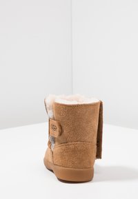 Bottines en suede marron avec une doublure douce, bout rond et détail de bouton sur le côté. Elles sont dotées d'une semelle en caoutchouc plate pour l'adhérence.