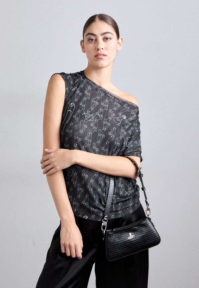 Top preto de manga curta com padrão de alfinetes de segurança brancos, design drapeado e decote ombro a ombro. Modelo segura uma bolsa texturada preta.