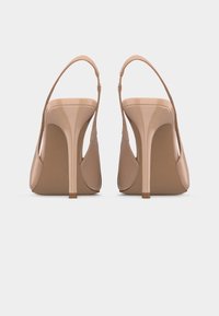 Para beżowych lakierowanych szpilek typu slingback z cienkimi obcasami typu szpilka, widzianych od tyłu na jednolitym białym tle.