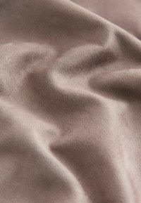 Tissu en suède doux de couleur mauve clair, drapé de plis doux avec des détails fins et texturés visibles à la surface.