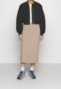 Černá bomber bunda s žebrovanými manžetami, béžová žebrovaná midi sukně a modré sportovní boty s multikolorovými akcenty a bílými ponožkami.