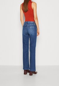 High-waisted blue denim jeans with a straight-leg cut, featuring back pockets and a clean finish. Worn with a fitted red top and brown block heels.