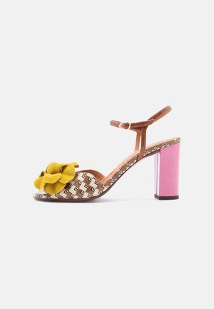 Pruun kontsaga sandaal kollase kangast õiega, mustrilise pealiskihiga, reguleeritava pahkluu rihmaga ja roosa ploki kontsaga. Kareda pinna ja avatud varbaga disain.