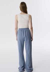 Top sin mangas de color beige claro combinado con pantalones de chándal sueltos de color azul claro que presentan tachuelas decorativas a lo largo de las costuras laterales y una cintura elástica.