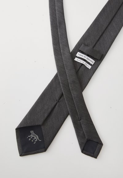 Siva kravata s uzorkom i teksturiranim finishom, s logotipom tigra na tamnoj fabrici oznaci i etiketom koja glasi "Tiger of Sweden - Made in Italy."