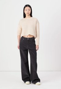 Beige cropped knit sweater with a loose weave, paired with high-waisted black corduroy wide-leg pants and cream-colored sneakers.