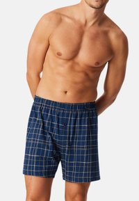 Boxers de hombre azules a cuadros con cinturilla elástica, que presentan un patrón de rejilla en blanco y beige. Fabricados con una tela suave y transpirable.