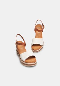 Sandali wedge bianchi e marroni con una larga fascia anteriore e una fascia alla caviglia. Texture in pelle liscia e soletta imbottita.