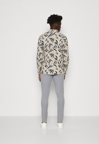 Langermet skjorte i beige med svarte bladmønstre, kombinert med lysegrå tettsittende bukser og hvite sneakers.