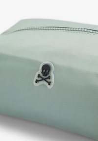 Funda rectangular de color verde claro con una cremallera en la parte superior y un pequeño emblema de calavera y huesos cruzados negros en la parte frontal.