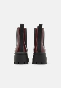 Bottines en cuir verni bourgogne avec des panneaux latéraux élastiques noirs et une semelle épaisse en noir. Comprend des languettes pour un enfilage facile.