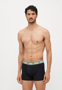 Black boxer briefs with a green Puma logo waistband. The fabric is smooth with a fitted design, providing support and coverage.