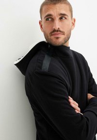 Felpa nera con colletto alto e foderato in pile bianco all'interno del cappuccio. Presenta un elegante accento a contrasto sulle spalle e chiusura a zip.