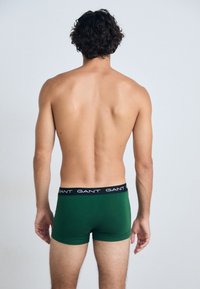 Shorts en coton verts avec une ceinture élastique noire portant le logo "GANT" répété, vus de dos.