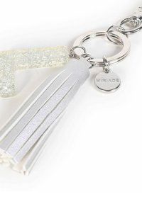 Portachiavi con una lettera 'G' chiara e luccicante, un tassello in pelle bianca e un anello circolare argentato con un piccolo tag inciso con la parola "MIRIADA."