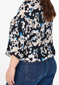 Blomstret bluse i sort, cremet og blå med trekvartærmer og en afslappet pasform, parret med denimjeans med baglommer.
