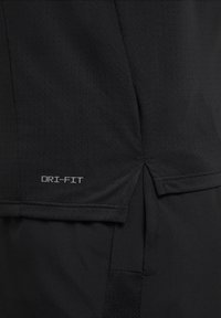 Gros plan sur un tissu sportif noir perforé avec une petite fente latérale et le texte « DRI-FIT » près de l'ourlet.