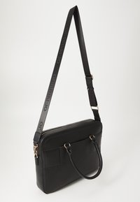 Sac à bandoulière en cuir noir avec ferrures dorées, double poignées et une longue sangle réglable avec marquage embossé. Texture lisse, forme rectangulaire.