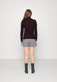 Maglione a collo alto scuro abbinato a pantaloni corti a scacchi grigi e bianchi. Modella con stivaletti neri con tacco, rivolta lontano dalla macchina fotografica.