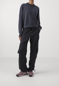 Sudadera gris oscuro con hombros caídos, combinada con pantalones de cargo negros con bolsillos laterales. Completada con zapatillas deportivas rosa claro.