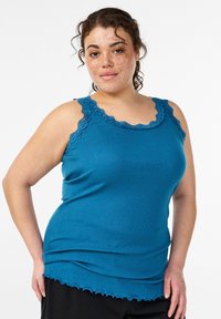 Türkisfarbenes, geripptes Tanktop mit gewelltem Spitzenbesatz an Schultern und Ausschnitt. Lockerer Sitz und welliger Saum. Weiche Textur.