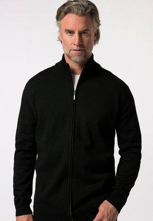 Schwarzer Strickpullover mit hohem Kragen, gerippter Textur und taillierten Ärmeln, mit einem silbernen Reißverschluss vorne.