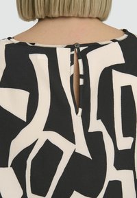 Black and cream patterned top featuring an open back with a small button closure. Textured fabric with bold abstract shapes.