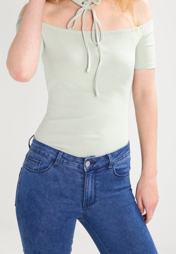 Ljusgröna off-the-shoulder bodysuit med korta ärmar, med en dragsko vid halsringningen, ihop med blå denimjeans.