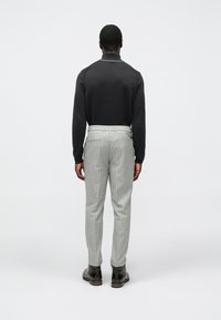 Črn pleten polo z dolgimi rokavi in ovratnikom je kombiniran s sivimi hlačami s črtami ter črnimi usnjenimi škornji, pogled od zadaj.