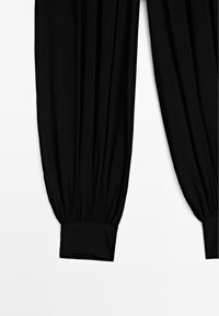 Schwarze Hose mit weitem Schnitt, gekennzeichnet durch gerafften Stoff, elastische Bündchen und glatte Textur. Keine sichtbaren Muster oder Hardware-Details.