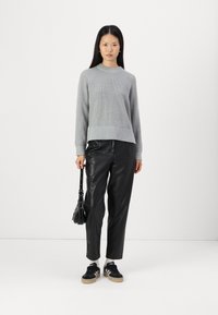 Maglione grigio lavorato a maglia con maniche lunghe, abbinato a pantaloni neri in ecopelle. Sneakers nere e una piccola borsa nera completano l'outfit.
