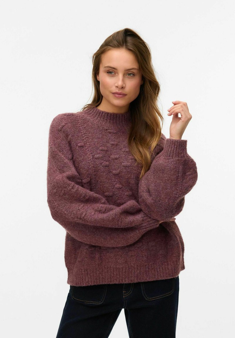 Pull-over en laine tricotée texturée de couleur prune profond, avec un col côtelé haut et des manches ballon, présentant des points en relief et un design épais et confortable.