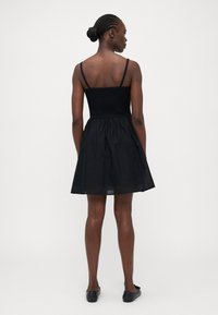 Vestido negro con un cuerpo ajustado y una falda acampanada, que cuenta con tirantes finos, espalda con fruncidos y una textura ligera.