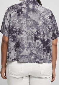 Camicia a maniche corte con colletto a punta, tagliata, in un motivo grigio e nero tie-dye, abbinata a pantaloni bianchi.