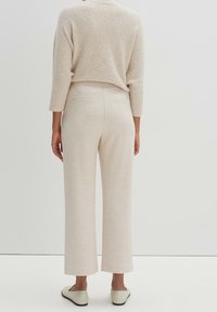 Suéter beige corto con una textura suave, combinado con pantalones sueltos de color claro que tienen bolsillos traseros y zapatos planos.