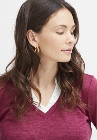 Maglione a V in tessuto a maglia bordeaux, indossato sopra una camicia bianca con colletto e bottoni. Caratterizzato da una consistenza morbida e una vestibilità rilassata.
