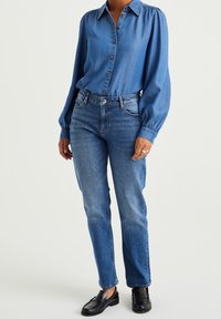 Two-piece outfit featuring a light blue denim shirt with buttons and puffed sleeves, paired with medium-wash straight-leg jeans and black shoes.