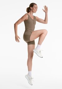 Hnedý pruhovaný športový tank top s detailom gombíka, zodpovedajúce vysoké šortky a biele športové topánky s textúrovanou podrážkou.